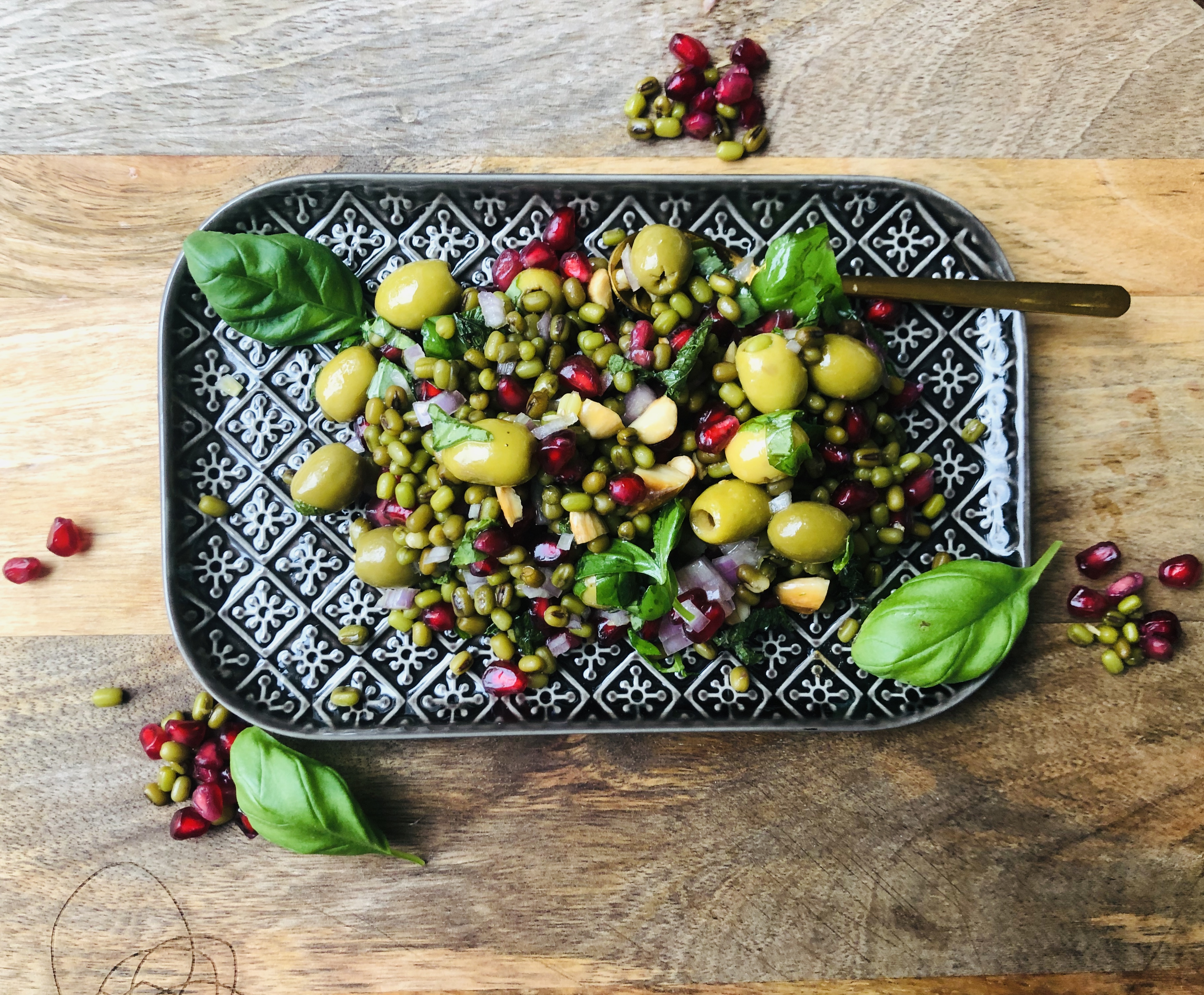 Mungbonensalade met groene olijven, granaatappelpitjes en groene kruiden